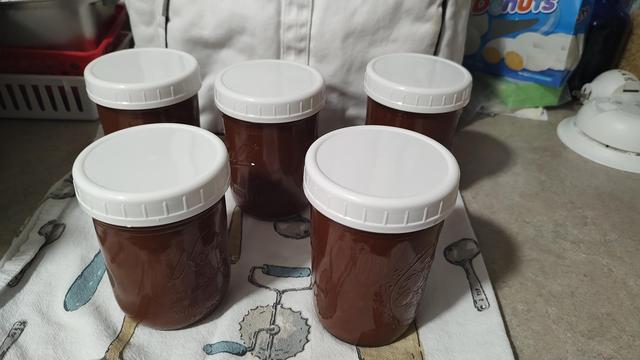 Five glass pint jars filled with delicious fresh apple butter. They're sitting on my kitchen counter, on a 40s-style kitchen towel decorated with antique kitchen tools.