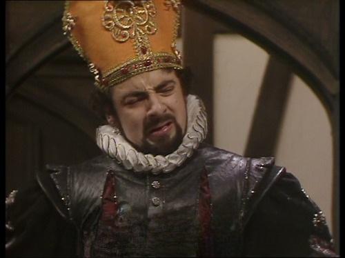 Edmund Blackadder as Cardinal Chunder from Blackadder 2. Set in Elizabethan times, he's in a black leather tunic with white ruff and wearing an ornate yellow cardinals hat.