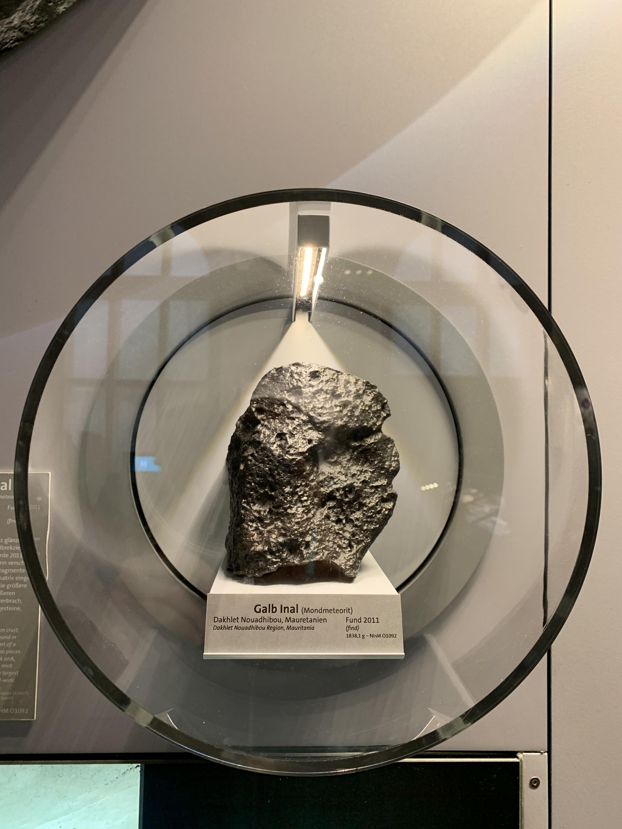 portal of a piece of meteorite in circular glass case in museum. text on pedestal reads:

Galb Inal (Mondmeteorit/moon meteorite)
Dakhlet Nouadhibou Region, Mauritania
Found in 2011