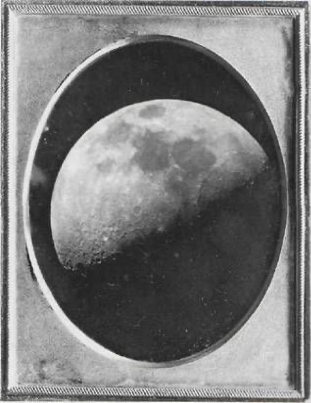 portal of an old black and white photo of the moon, half in shadow. the photo is inside a picture frame with an oval cut-out inner frame.