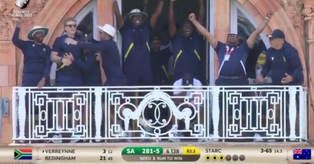 A group of South African male cricketers and coaches on an ornate balcony at Lord's cricket ground. All but one of them is in dark blue clothing and celebrating uproariously. In the middle, one (Temba Bavuma) sits, still in his white playing gear, head down and in his hands.
At the bottom, the score shows that South Africa need 1 run to beat Australia (but in fact that run has just been scored, hence the celebration).