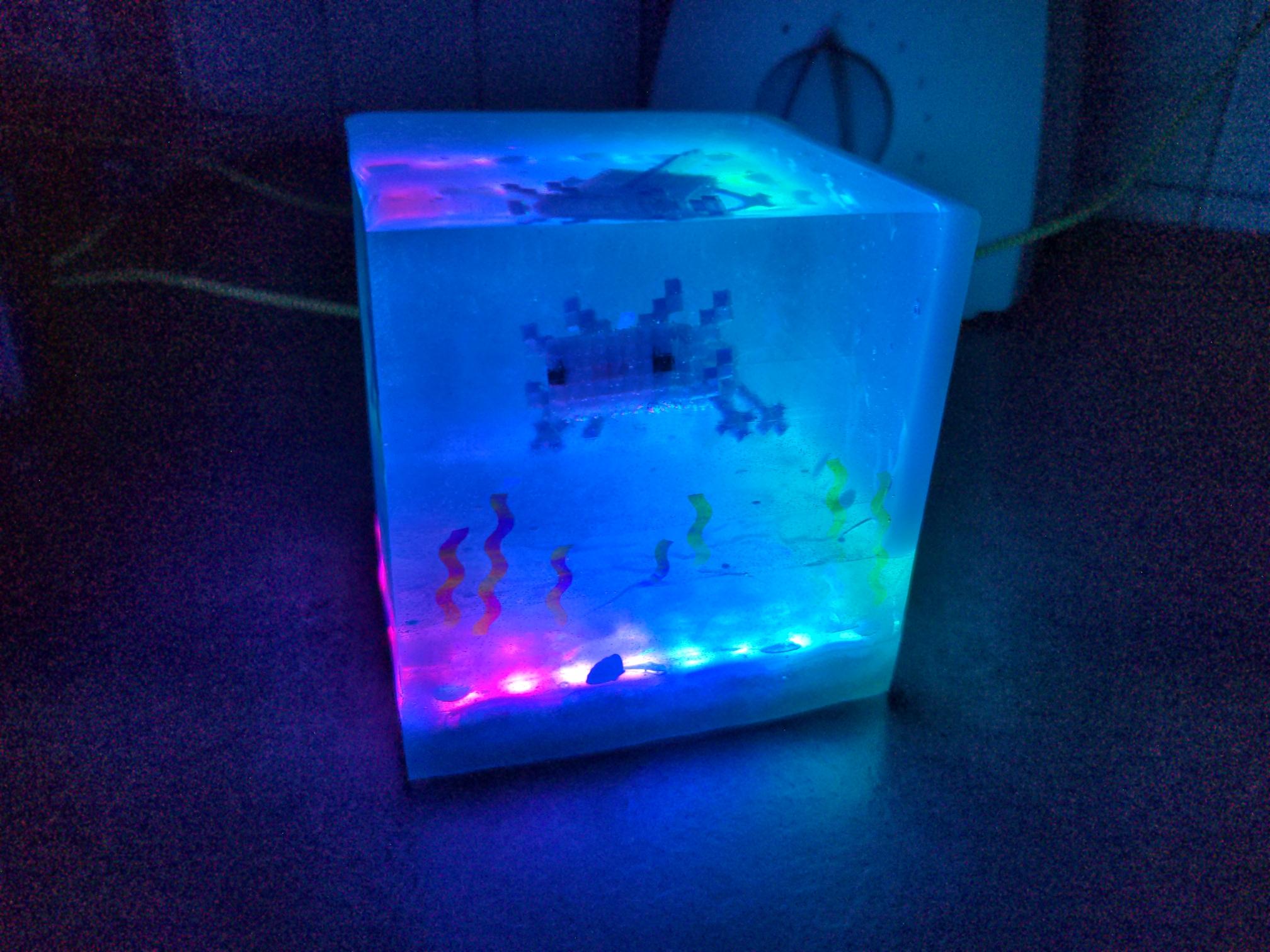 front view of the cube, LEDs glowing pink and blue with the axolotl looking at the camera