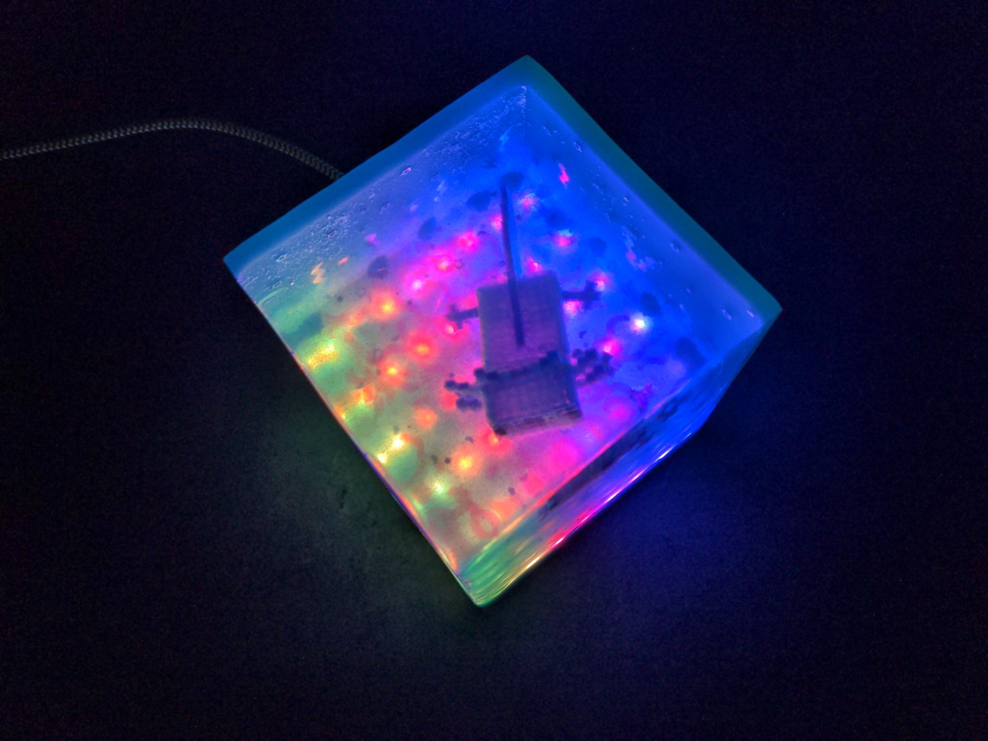top down view of the cube showing a grid of LEDs glowing green, red, pink and purple and the axolotl swimming above it