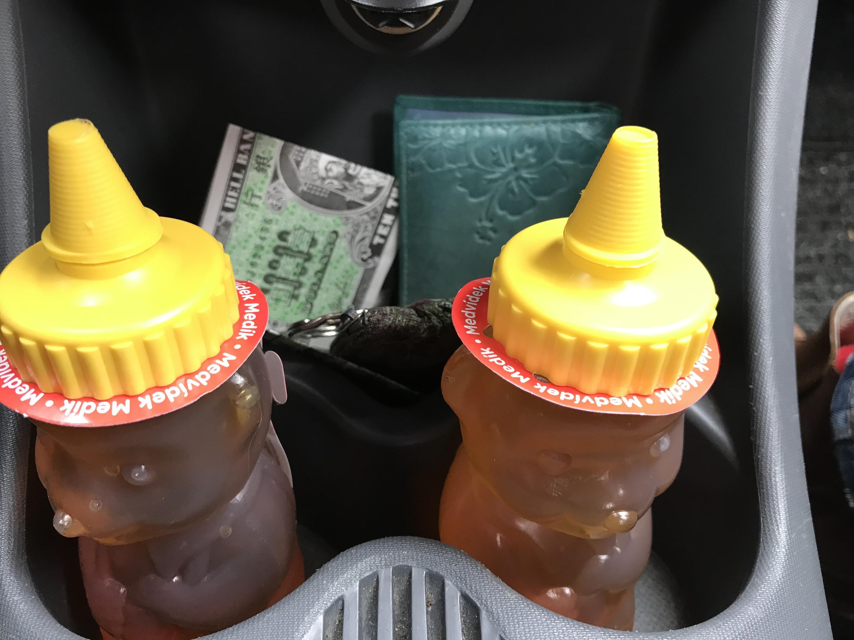 two honey bears in car drink holder slots. their caps are yellow, their bodies amber. behind them fake money (hell notes) to be burned at new year’s eve celebrations and an aqua-colored leather wallet.