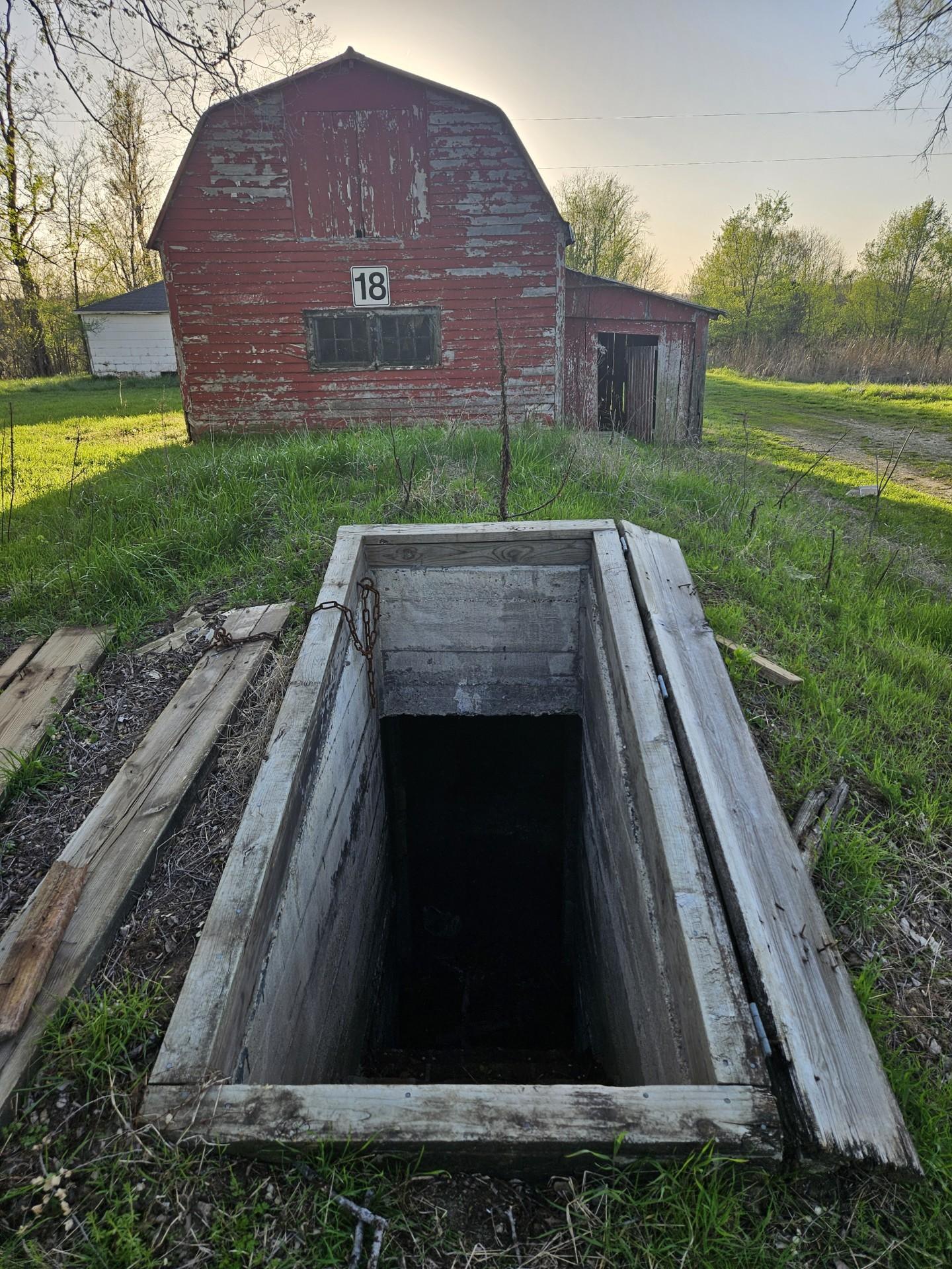 A dark concrete opening of a cellar with a red barn in the background 