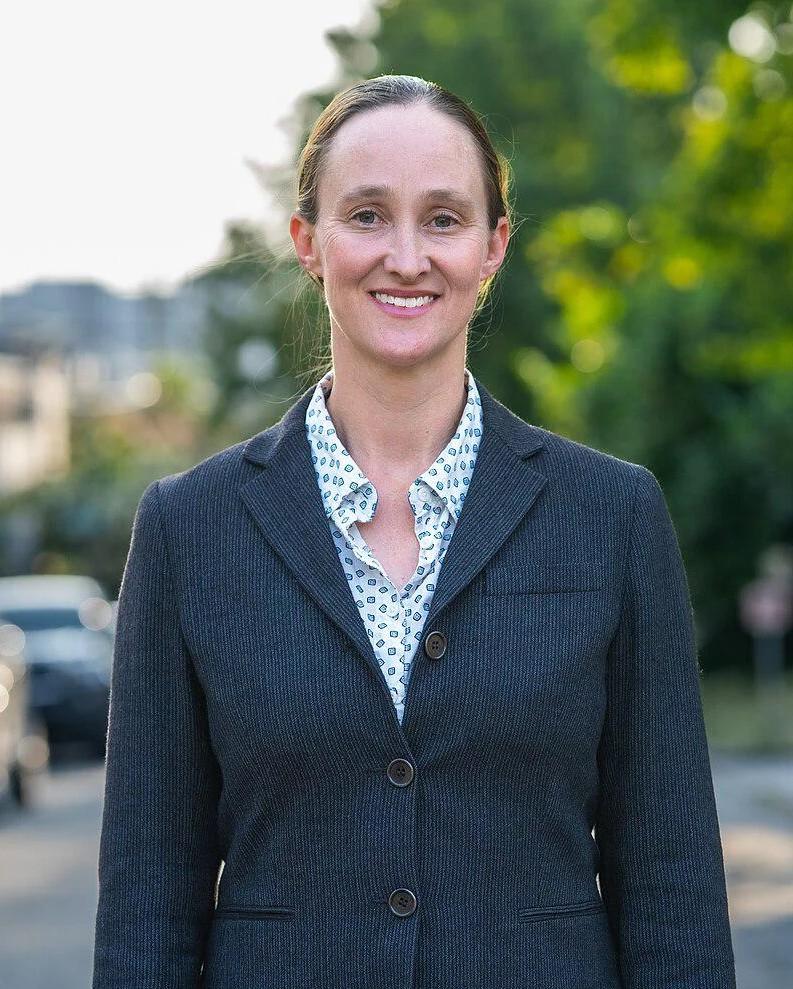 A white woman with hair pulled back and a smart business suit with a polka dot shirt underneath