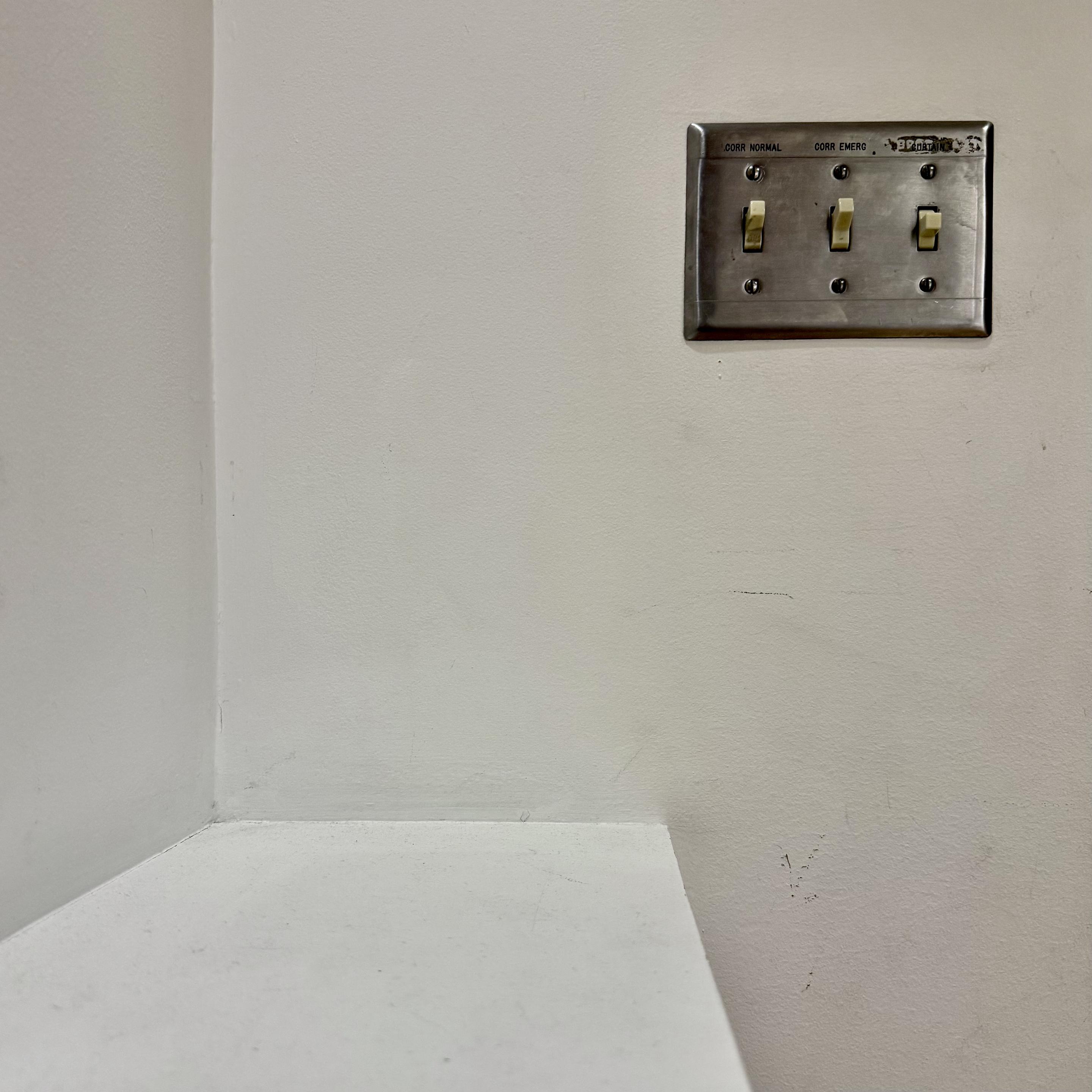 Vintage light switch with a silver-aluminum/stainless steel switch plate in the corner of an art museum.