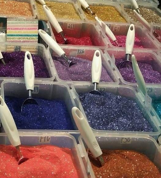 A table full of big plastic containers of glitter with big scoops in them