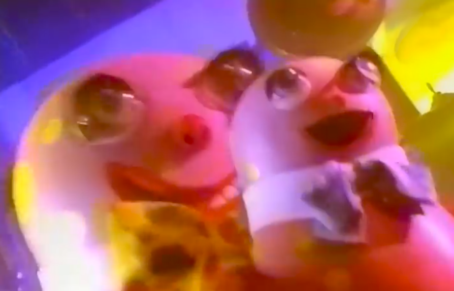 The UK Mr. Bobby, pink bipedal inflated costume of blob, shame, and sin, holding up a young child Blobby.