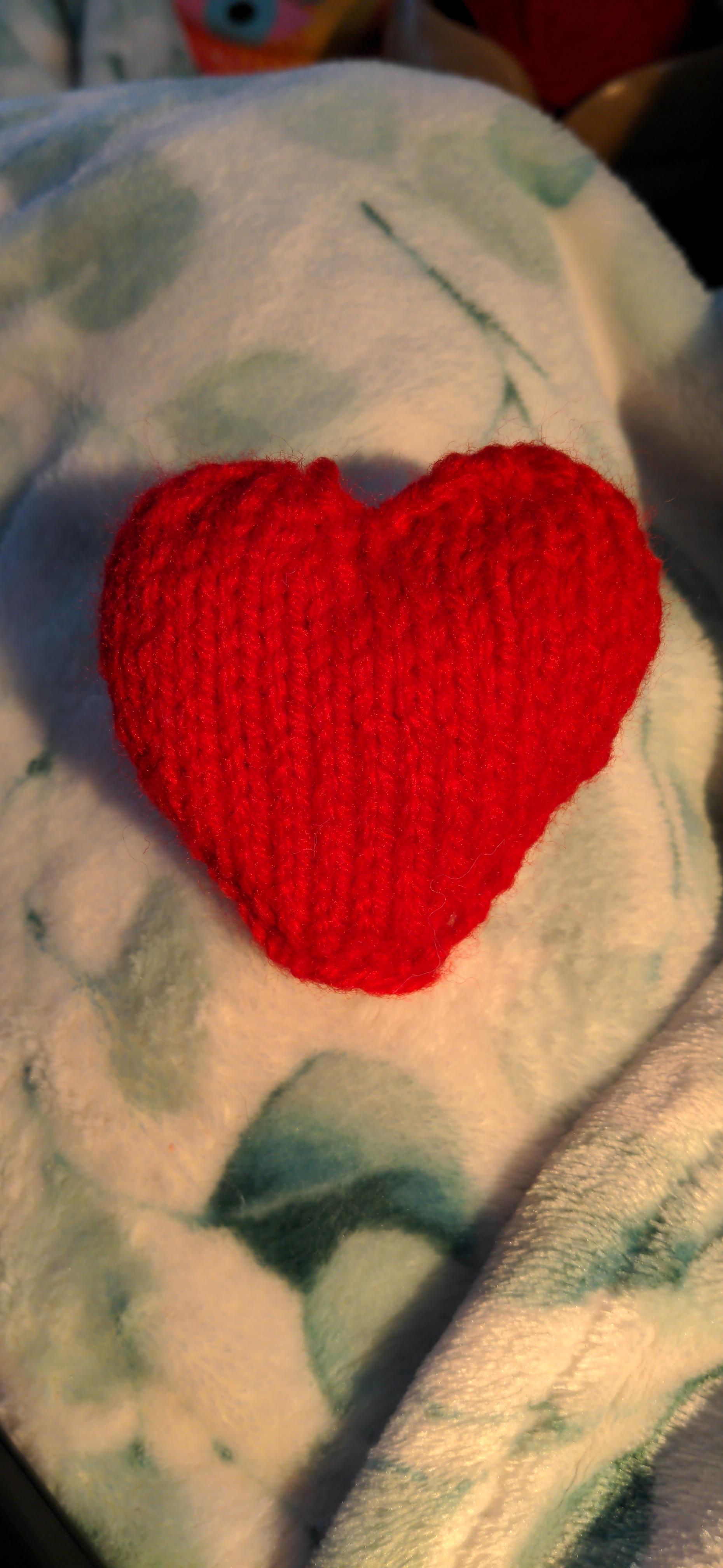 A lovingly-made, slightly lumpy knit heart in a vibrant red yarn.