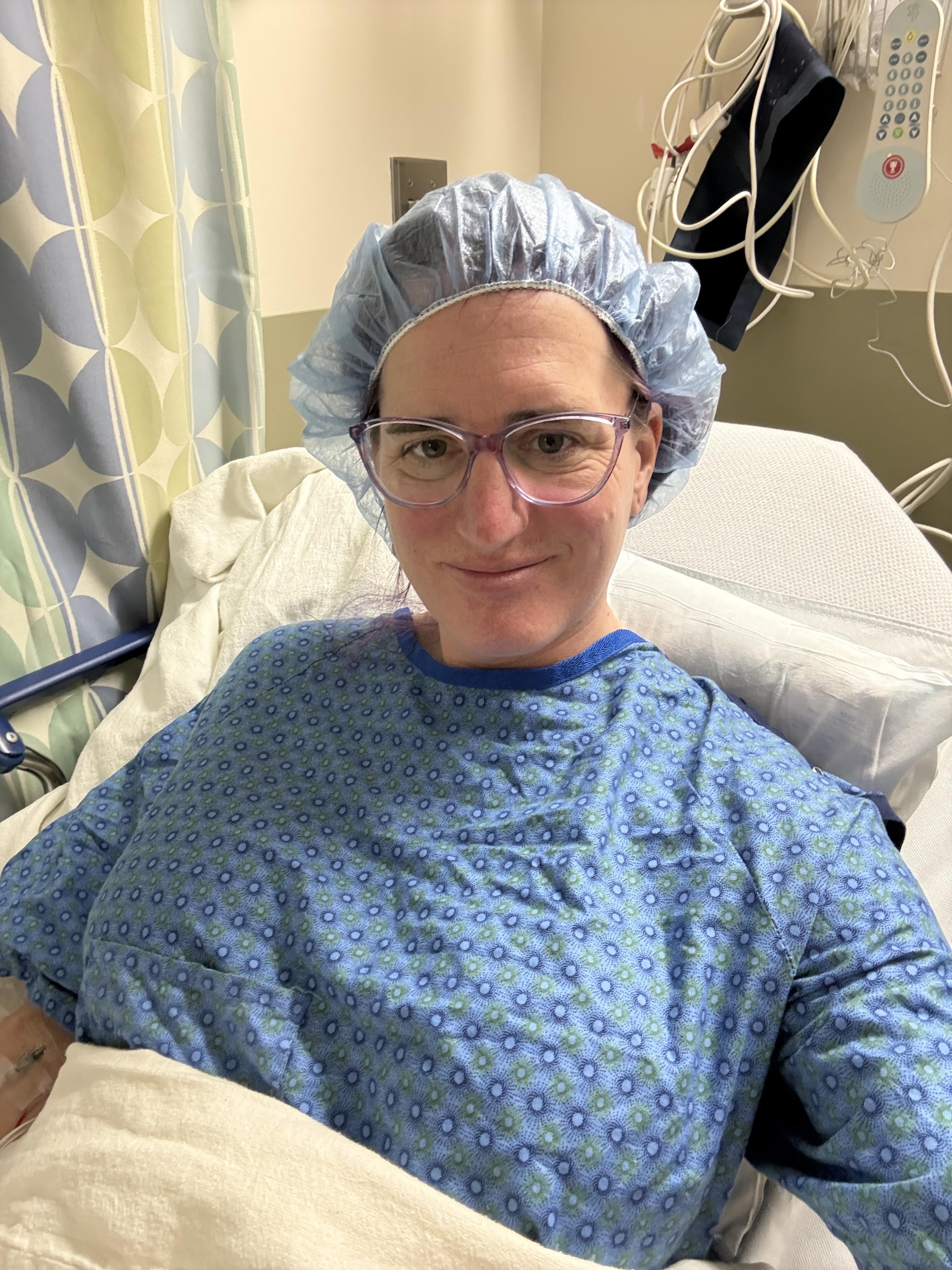 Selfie of a lady wearing a hospital gown laying in a hospital gurney.