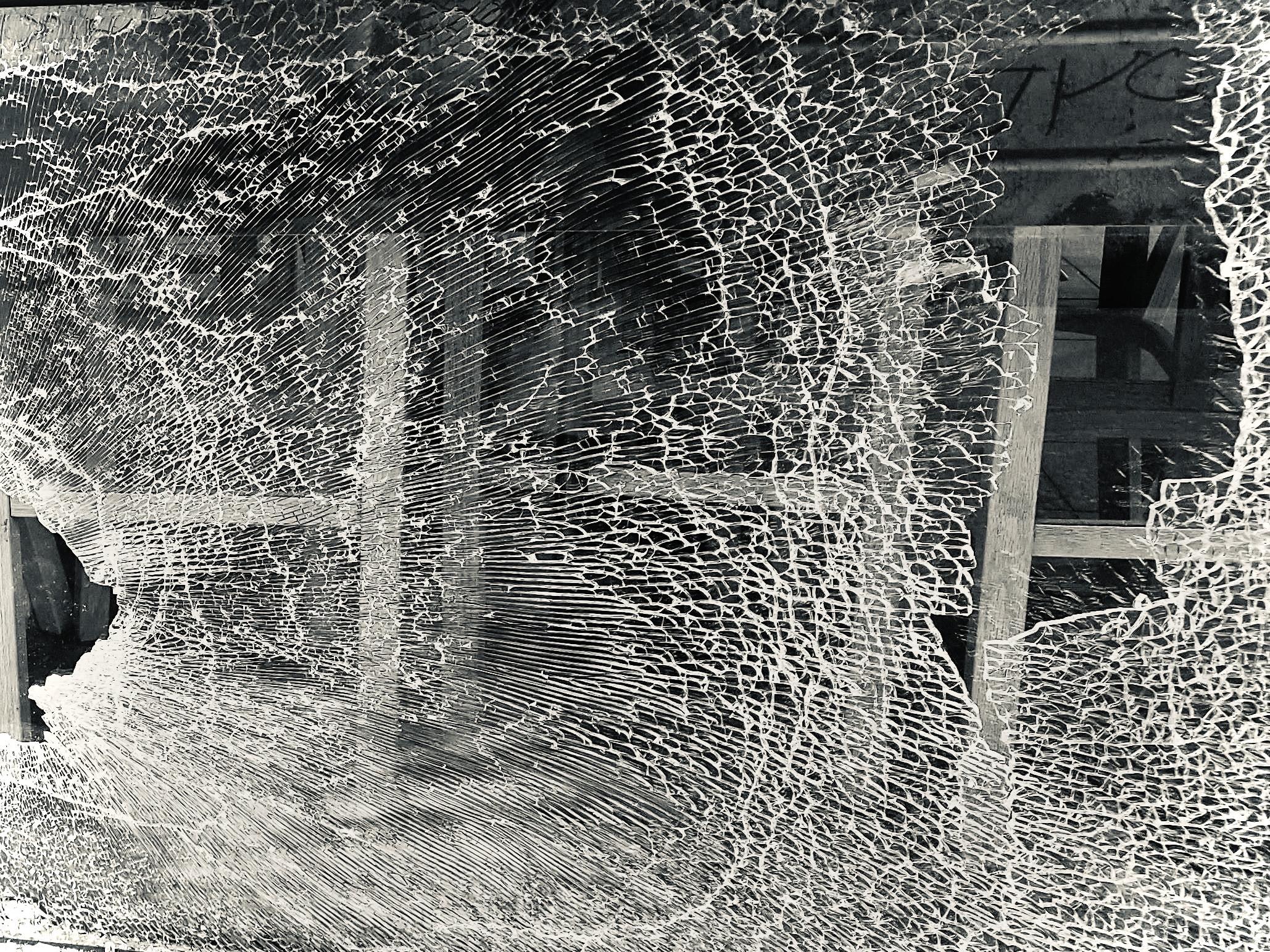 Broken window that had thousands of hairline cracks that make a wave pattern almost like a spiderweb. You see into the bar where there are wood stools or chairs. It’s still holding together mostly and must be safety glass. Image has been cropped from Mike’s photo and a filter for Silvertone applied, edited on iPhone.
