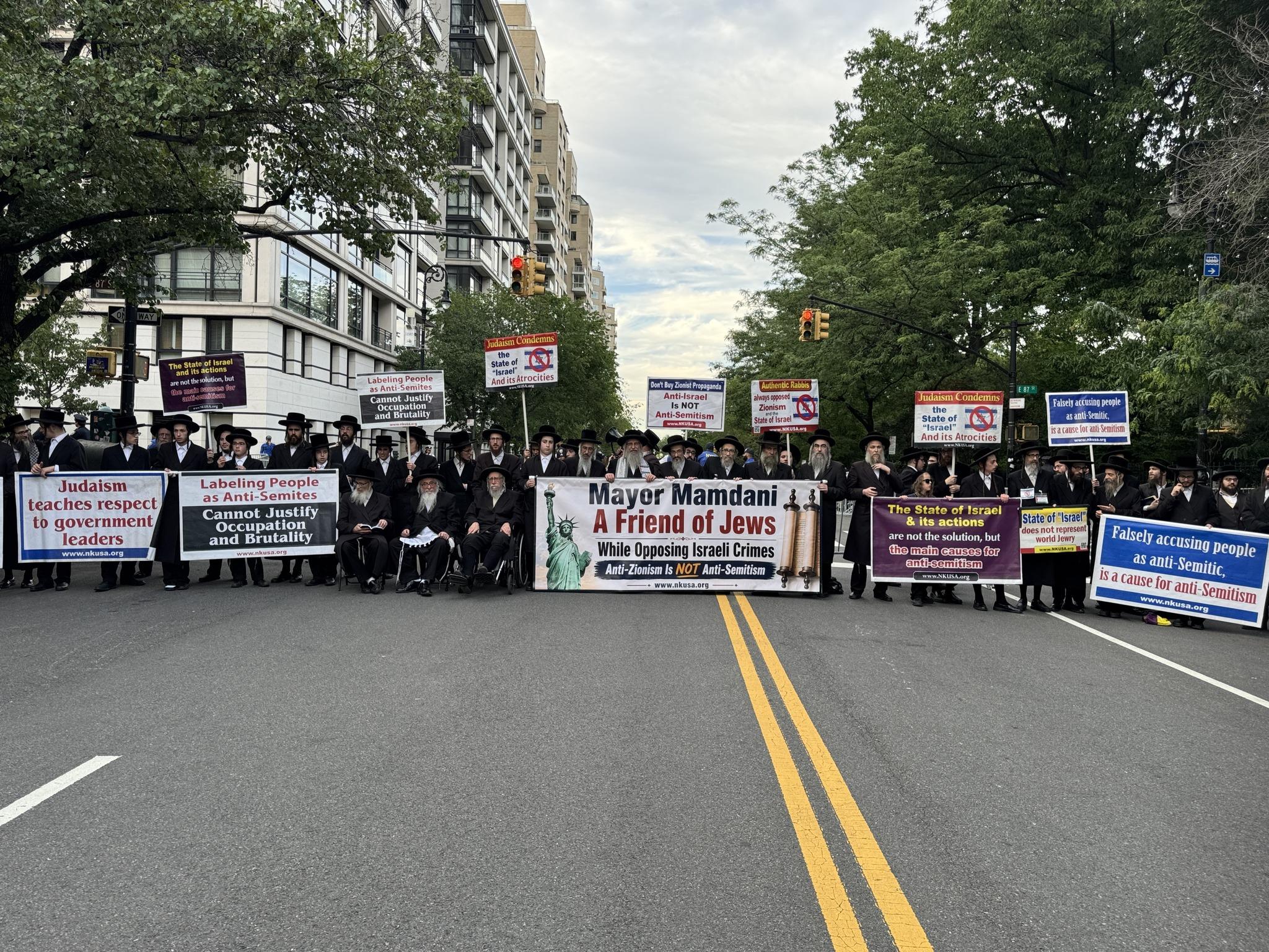 Photo of Jewish rabbis blocking a street in New York in protest, holding sign footnoted with the web address of www.nkusa.org that contain messages like, "Mayor Mamdani - A Friend of Jews, While Opposing Israeli Crimes. Anti-Zionism Is NOT Anti-Semitism", "Anti-Israel is NOT Anti-Semitism", "Authentic Rabbis always opposed Zionism and the State of Israel", "Judaism Condemns the State of 'Israel' And its Atrocities", "Falsely accusing people as anti-Semitic, is a cause for anti-Semitism", "The State of Israel & its actions are not the solution, but the main causes for anti-semitism", "State of 'Israel' does not represent world Jewry", "Labeling People as Anti-Semites Cannot Justify Occupation and Brutality", and "Judaism teaches respect to government leaders".