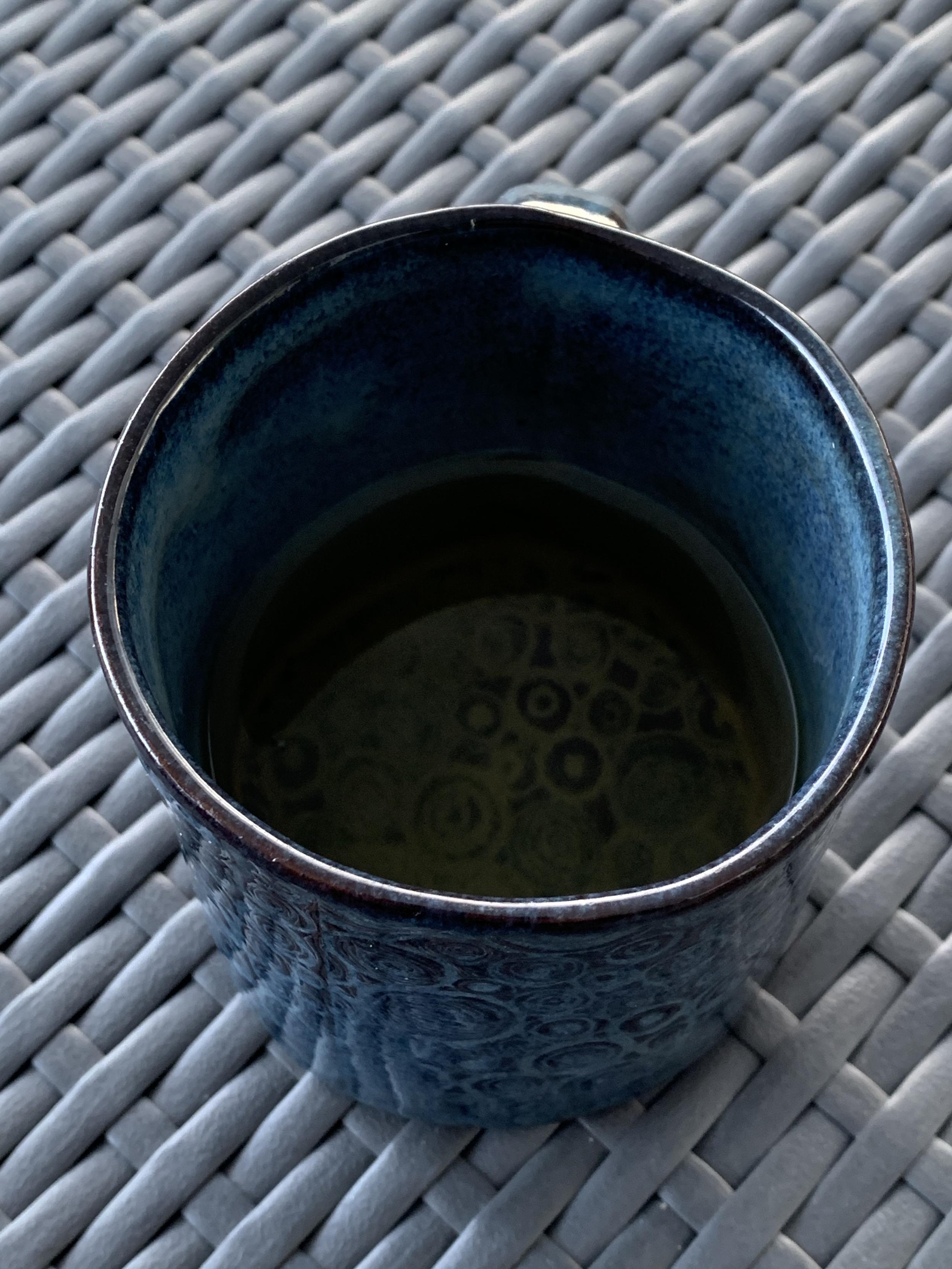 blue ceramic coffee mug on gray plastic rattan. the surface of the mug’s sides and bottom are covered with swirls in the clay/glaze.