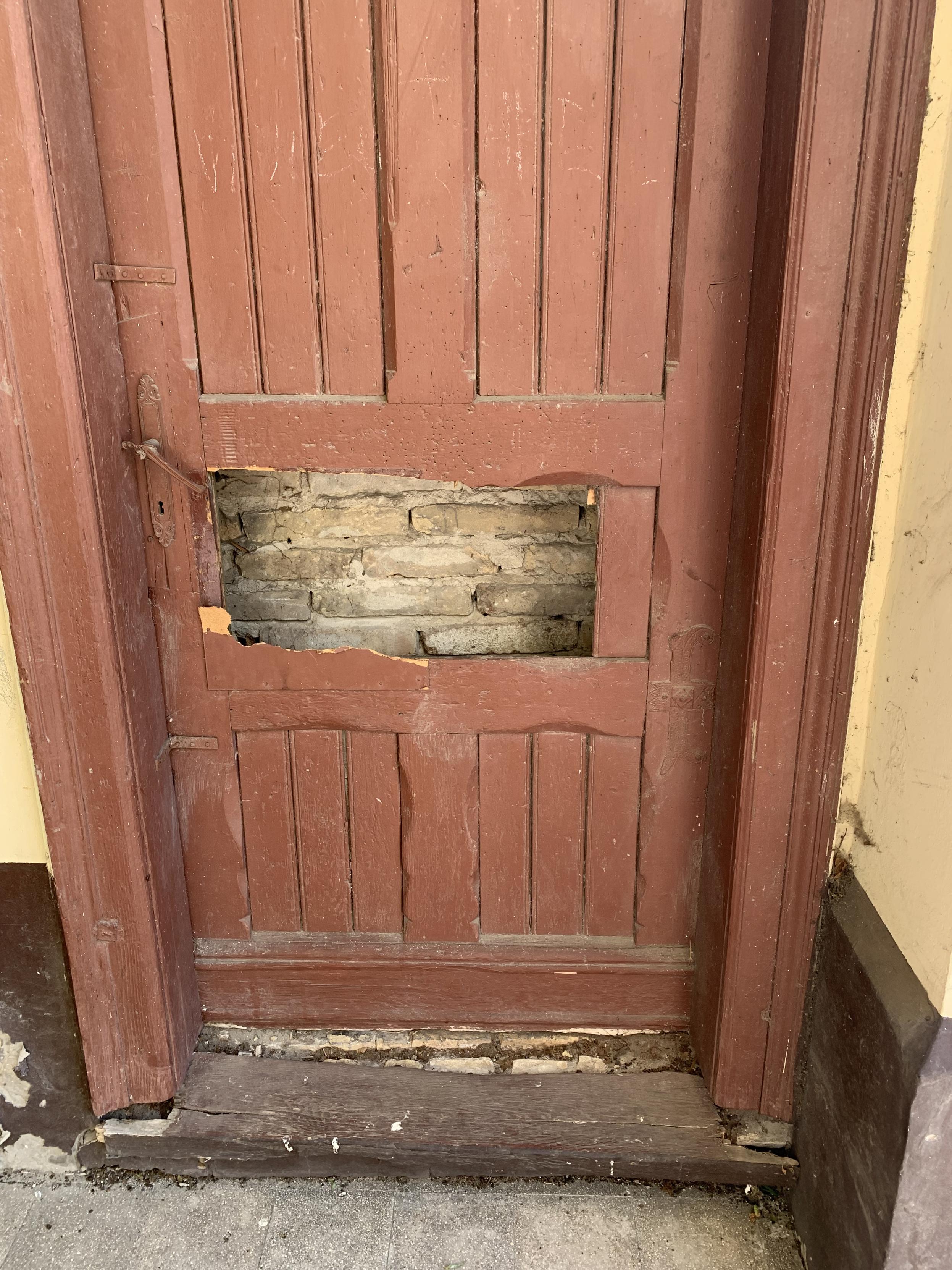 brown wooden door with missing panel leading to bricked up wall behind it.