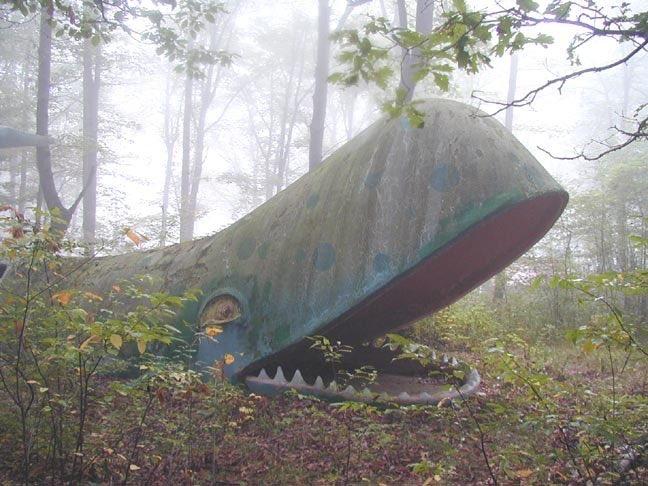 Whale sculpture covered with moss in woods, mouth wide open — source unknown