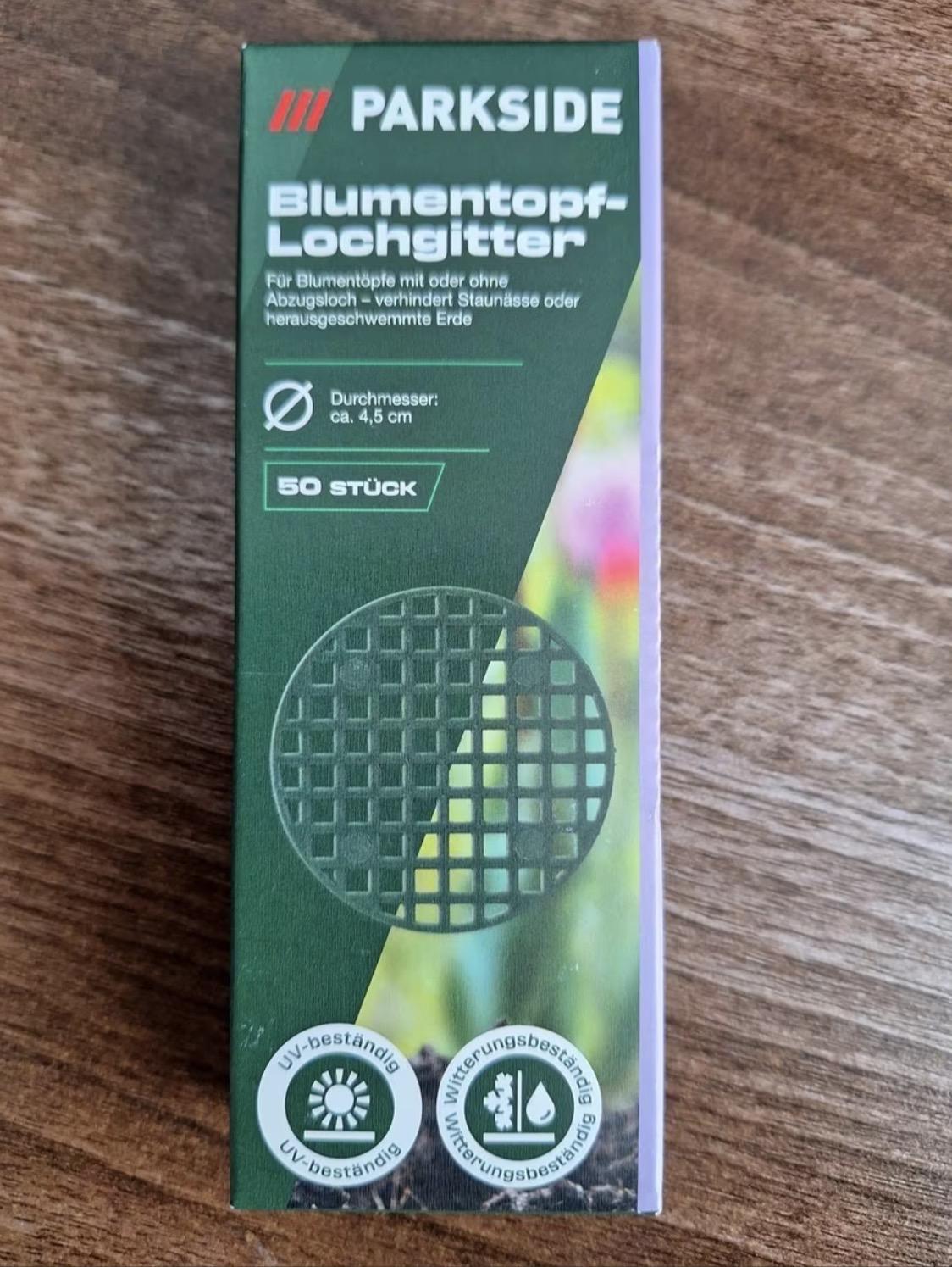 Ein vertikales, rechteckiges Produktpaket steht auf einer Holzoberfläche. Am oberen Rand befindet sich das Logo „PARKSIDE“ neben drei schrägen Linien in Blau, Rot und Orange. Der Titel lautet „Blumentopf-Lochgitter“, ergänzt durch den Text „Für Blumentöpfe mit oder ohne Abzugsloch - verhindert Staunässe oder herausgeschwemmte Erde“. Es folgen die Angaben „D „Durchmesser: ca. 4,5 cm“ sowie „50 STÜCK“. Auf dem Paket ist ein schwarzes, kreisförmiges Gitter vor einem unscharfen Hintergrund abgebildet sowie zwei Siegel am unteren Rand mit der Aufschrift „UV-beständ „UV-beständig“ und „Witterungsbeständig“.