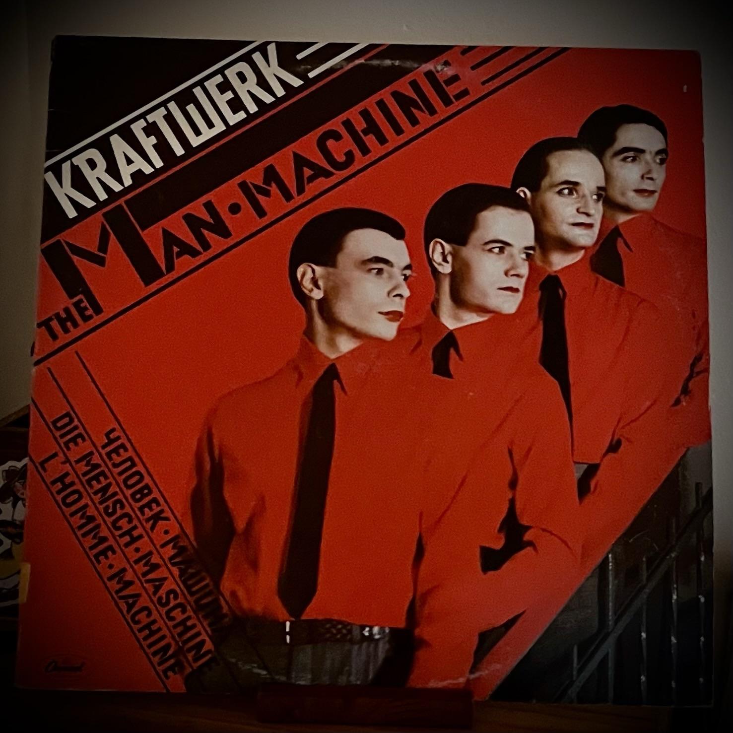 Album cover for "The Man-Machine" by Kraftwerk features four members in red shirts and black ties against a bright red background. The title and band name are prominently displayed in a stylized font.