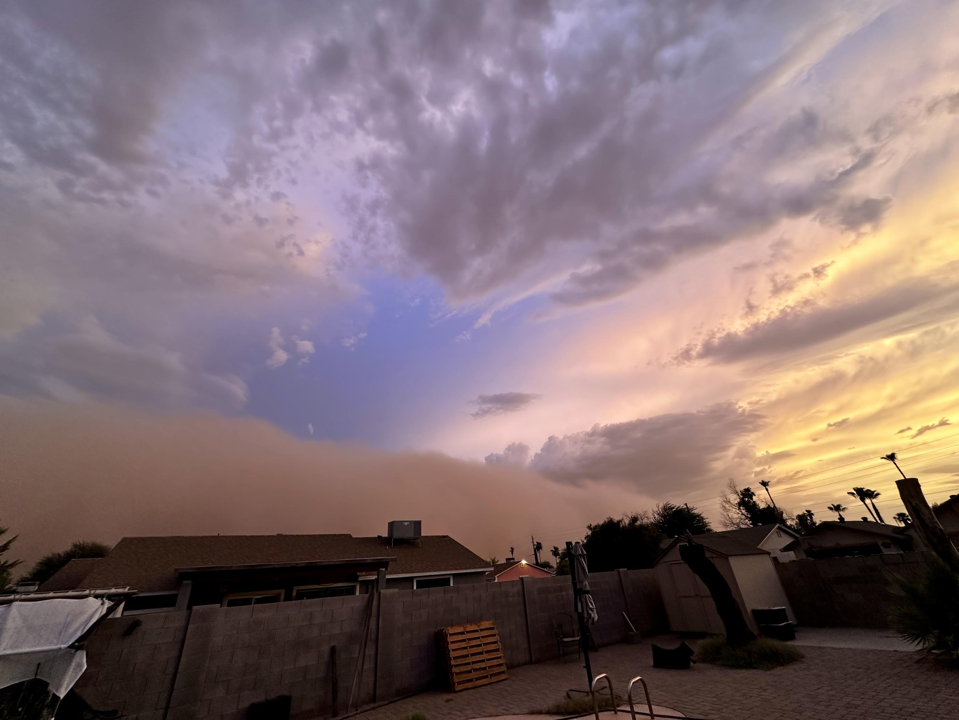 Looks pretty, yes? NOPE This is a dust storm rolling in fast from south to north there will be spectacular photos on the news tonight and tomorrow. This skyscape photo from our backyard is 3/4 sky and clouds. Lowest is rooftops and treetops of neighbors. Blue sky no clouds in center. To right is west and glowing yellow with reds. To left is towards downtown. This photo taken about 20 minutes ago and it’s all brown-gray here now.