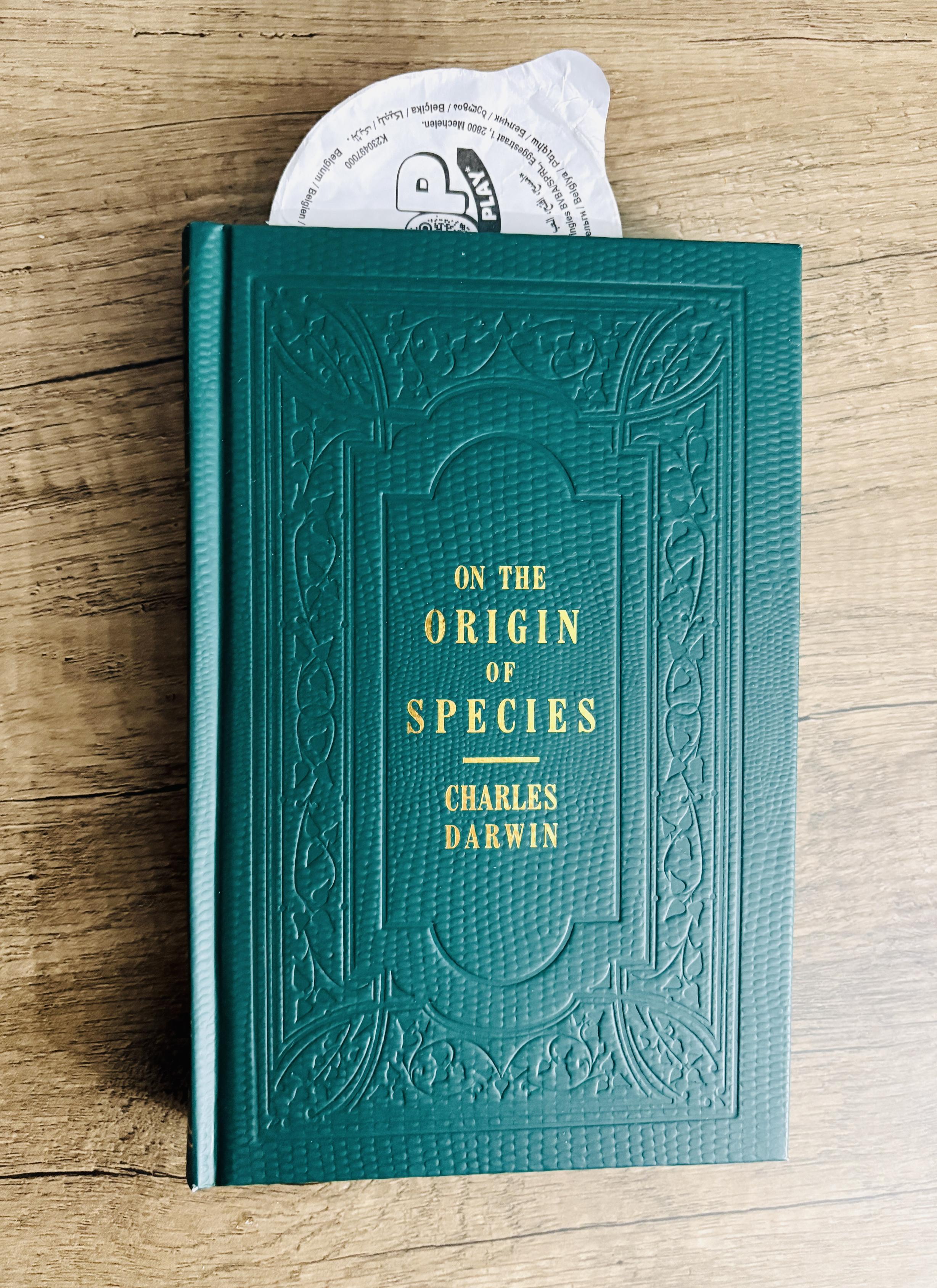 A hardback copy of 'On the Origin of Species' with the seal thing from a Pringles tube as a bookmark