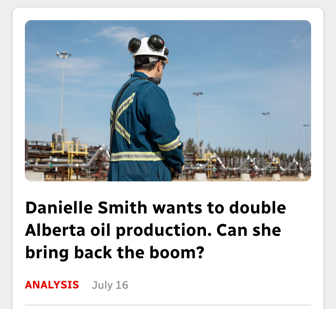 photo of an worker in blue safety coveralls with a helmet on with their back to the camera, looking at an elaborate pipeline system against a backdrop of a blue nearly clear sky. Headline: Danielle Smith wants to double Alberta oil production. Can she bring back the boom?