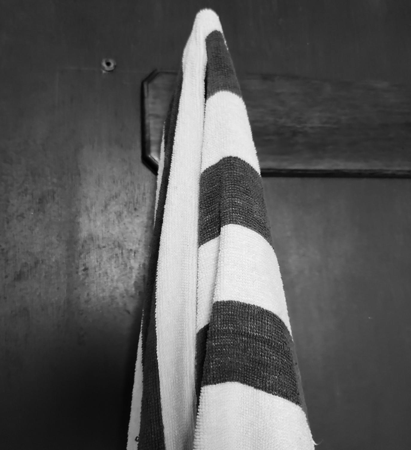 A black and white striped towel hangs from a hook on a dark wooden bathroom door surface.