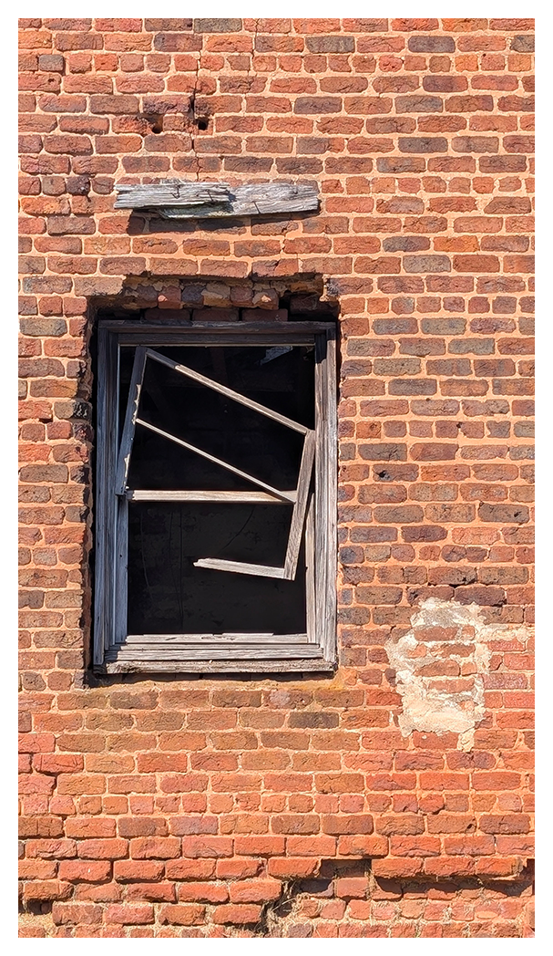 a damaged brick wall features a broken wooden window frame with crooked bars. The bricks are reddish-brown, some sections are chipped, and mortar is missing in places. There's a patch of lighter, repaired bricks below the window.