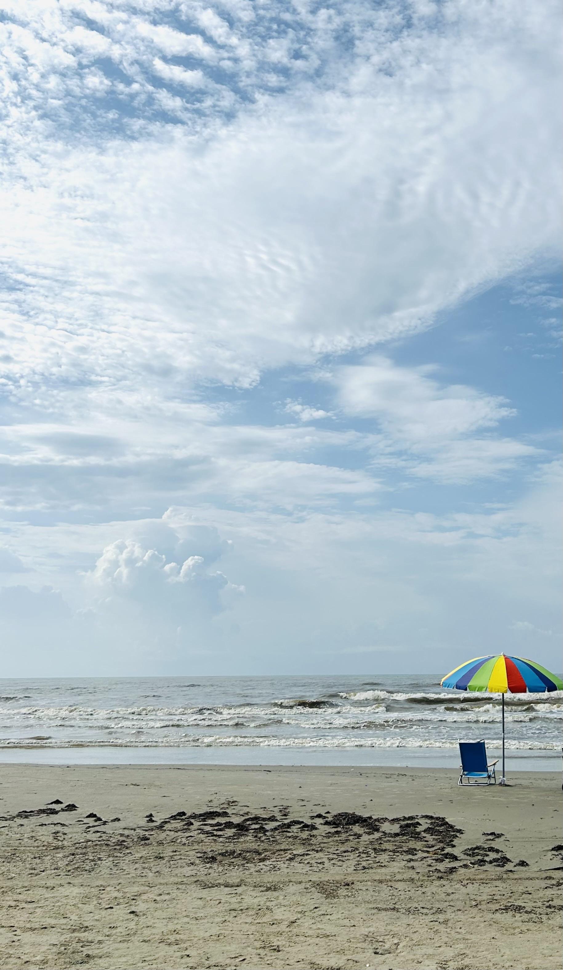 One blue chair next to a brightly colored umbrella on the beach