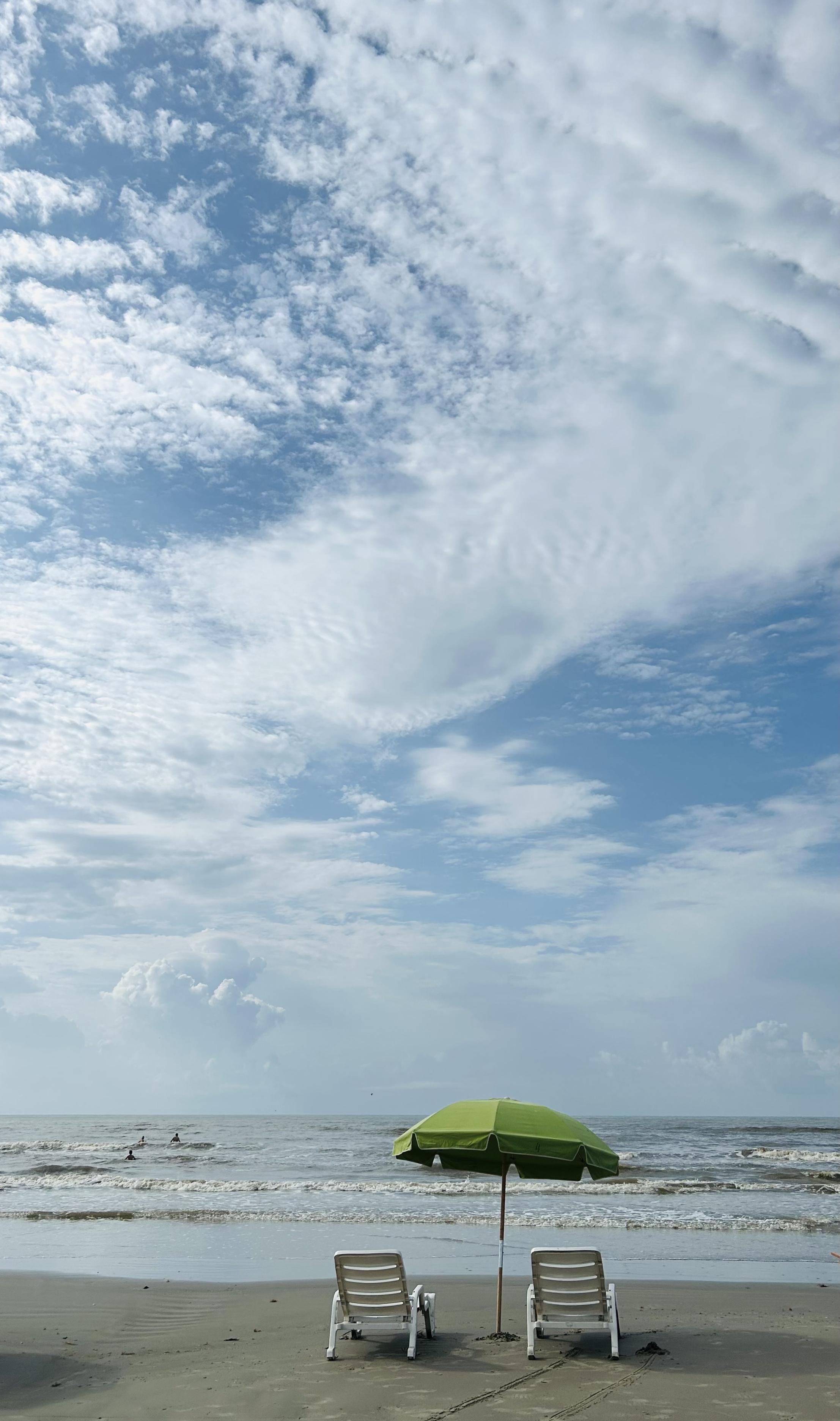 Two white chairs and a green umbrella facing the ocean