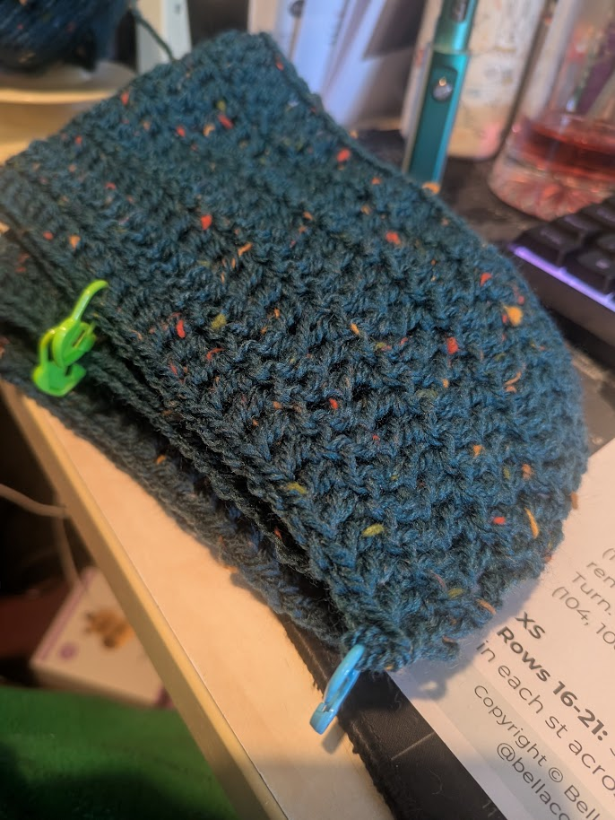 A pile of crochet, the yarn is Ocean, a deep green colour with flecks of red, yellow, light green and orange through it.