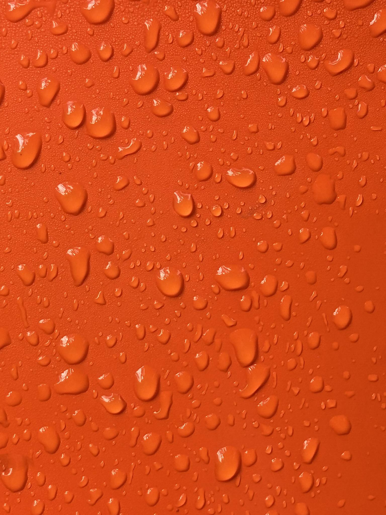 A bright orange surface covered in water droplets, some of which are glinting with reflected sunshine.