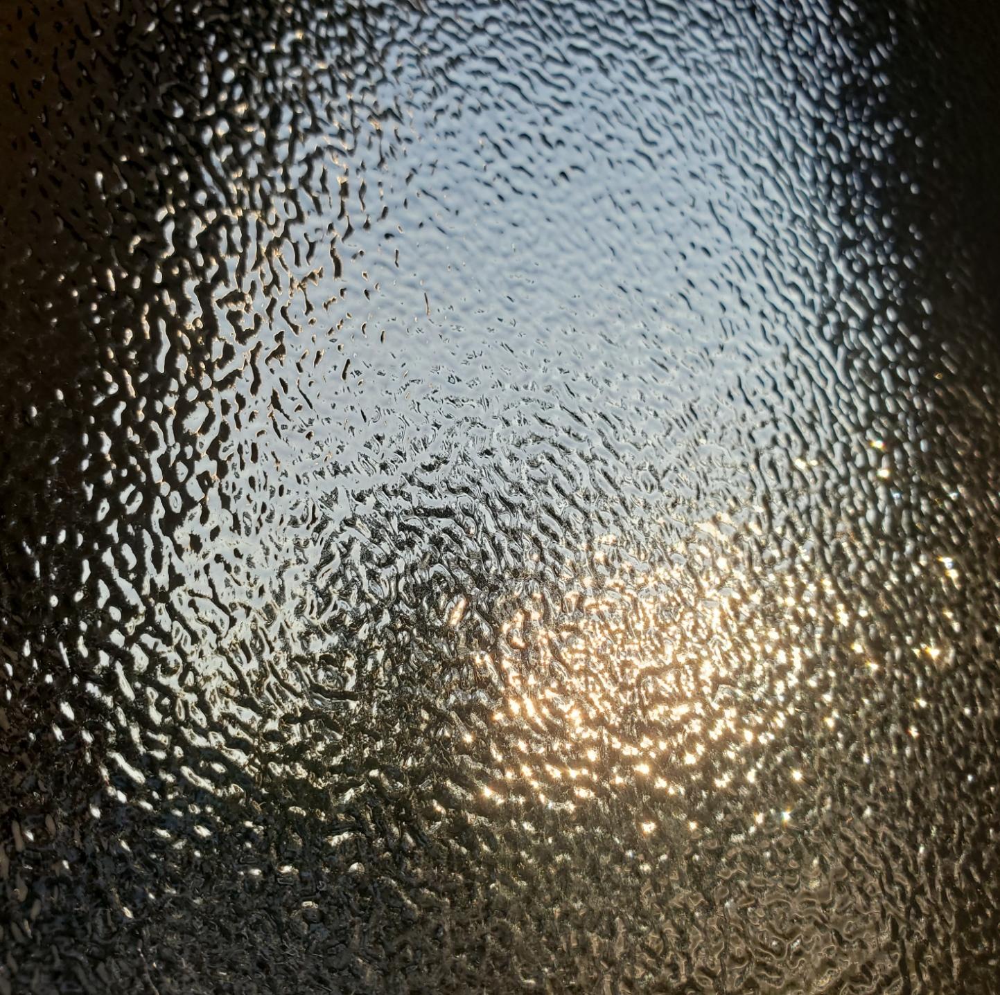 Close-up abstract texture of textured glass with sunlight filtering through and creating a bright, rippled glow.