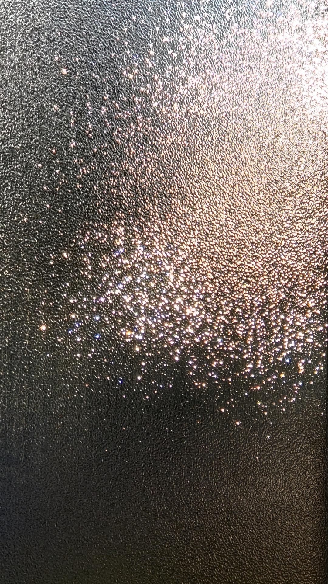 Close-up of a textured, frosted glass surface with bright highlights reflecting light, creating a sparkling effect against a darker background.