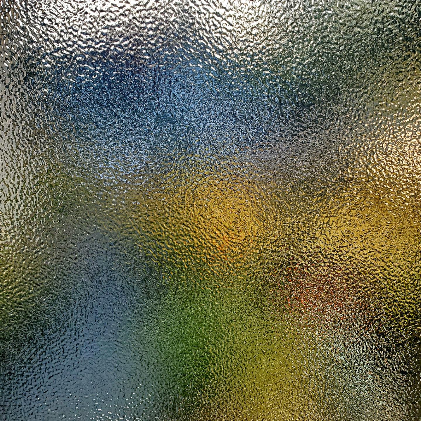 Abstract textured glass distorts a colorful outdoor scene with bands of blue, yellow, and green.
