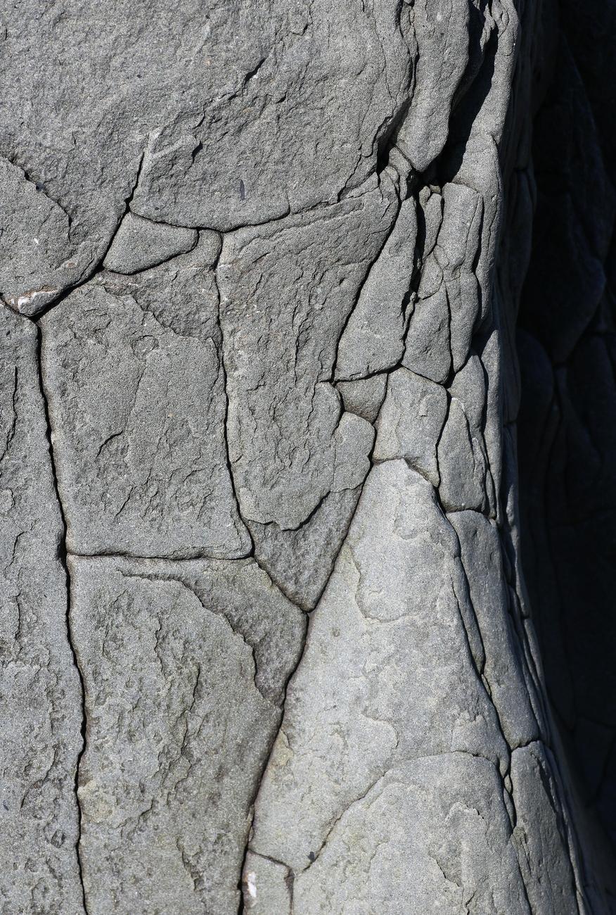 Close-up photograph of a grey rock, taken from above, its flat surface in the sun and divided into plates by deep cracks, and its right side plunging into shadow.

Photographie en gros plan d'un rocher gris, prise du dessus, sa surface plane au soleil et divisée en plaques par des fissures profondes, et son côté droit plongeant dans l'ombre.