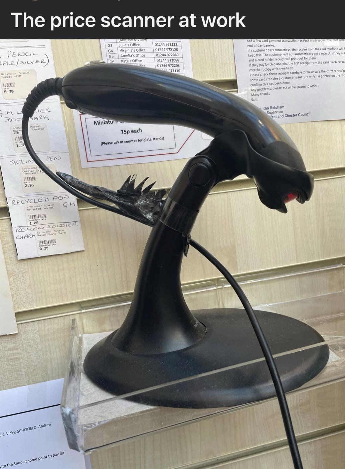 A black price scanner shaped like an Alien from the 1979 movie (with the addition of spikes on the back) sits on a stand. The text reads: "The price scanner at work".